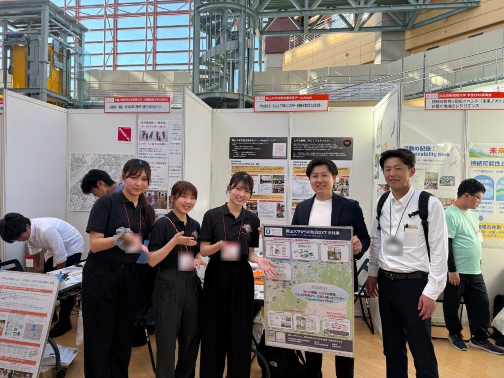 ぼうさいこくたい2026のAegisブースで、防災DXのポスターを手にする学生と代表の平山