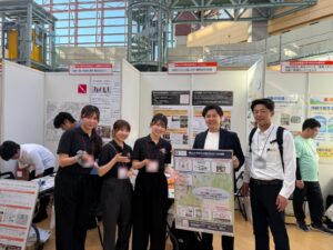 ぼうさいこくたい2026のAegisブースで、防災DXのポスターを手にする学生と代表の平山